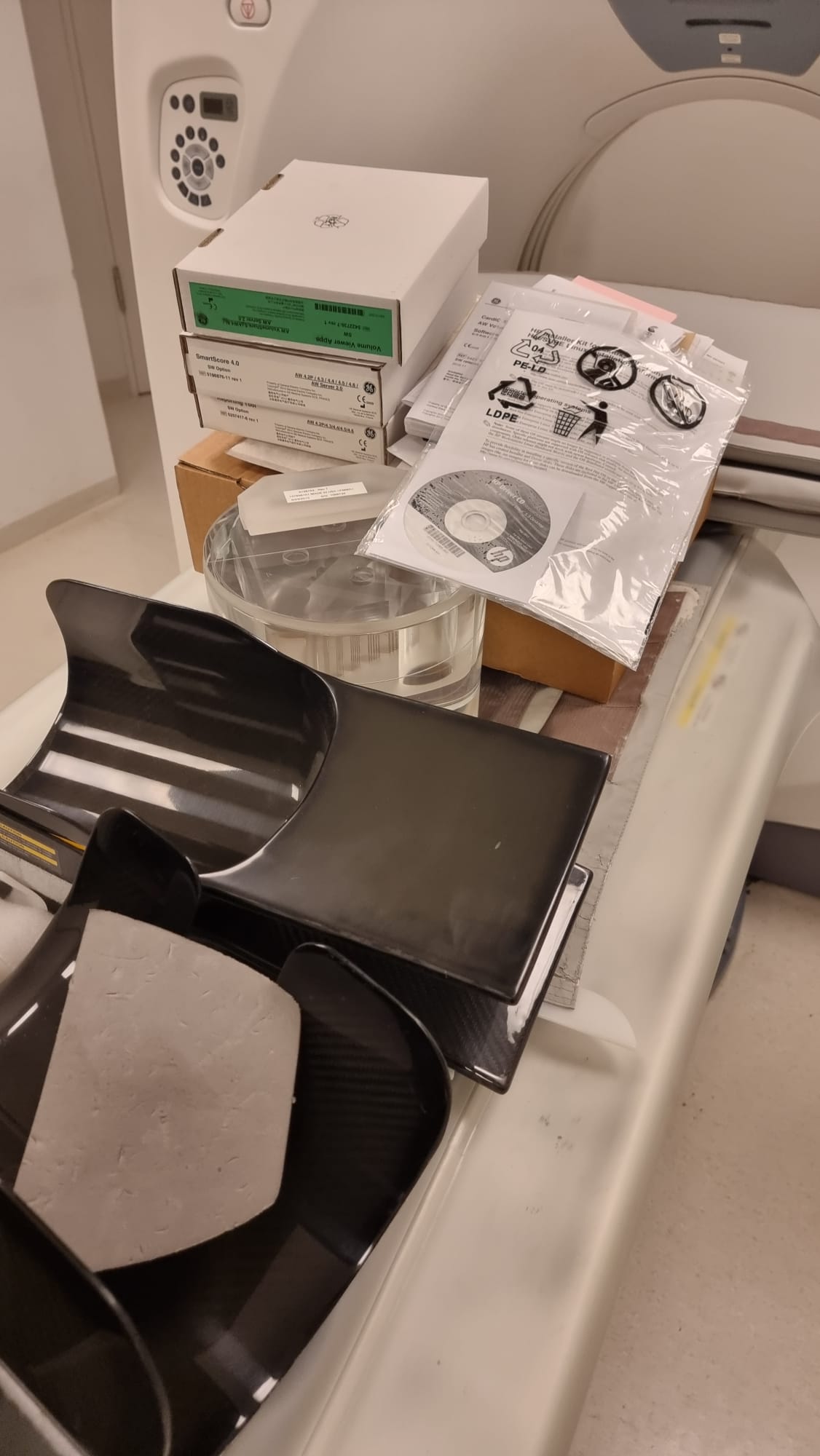 GE Optima CT660 original OEM software-option media — GE SmartScore 4.0 SW Option, AW Volume Viewer Appx AW Server 2.0 and Reporting Tool SW Option boxes photographed with calibration phantom and carbon-fiber head holders at MTC Miami, Florida