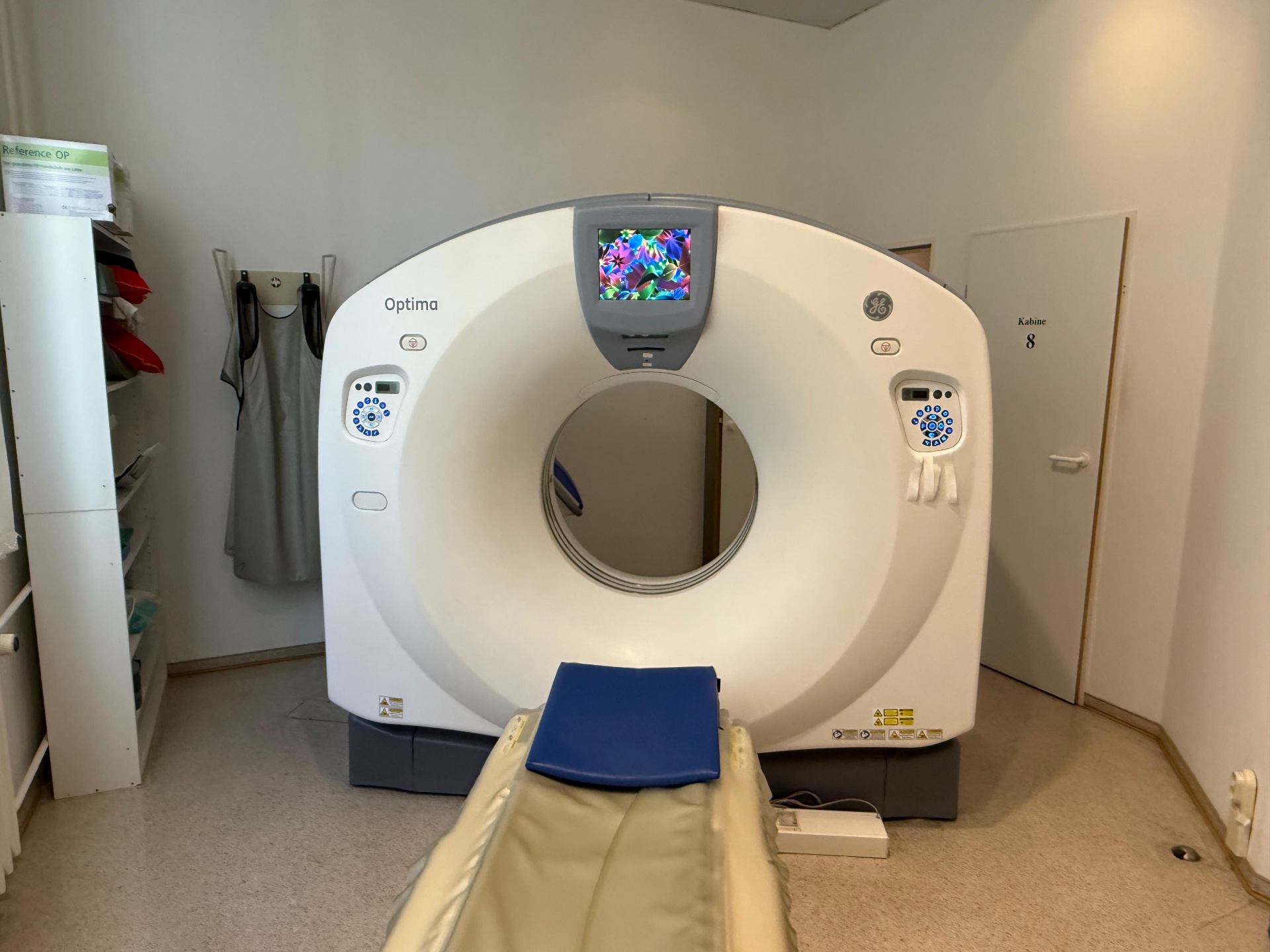 GE Optima CT520 gantry front view with operator touch panels, bore and patient table visible