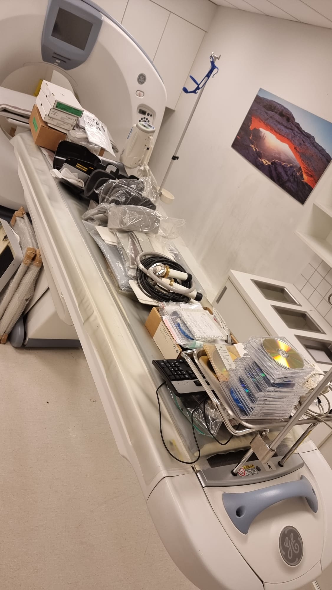GE Optima CT660 128-slice CT scan room view — Optima gantry with patient table loaded with head holders, phantoms, cables and Performix 40 Plus tube assembly ready for MTC packing in Miami, Florida